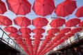Many Red Coral Umbrellas Against The Blue Sky And The Bright Building. Abstract Background With Umbrellas